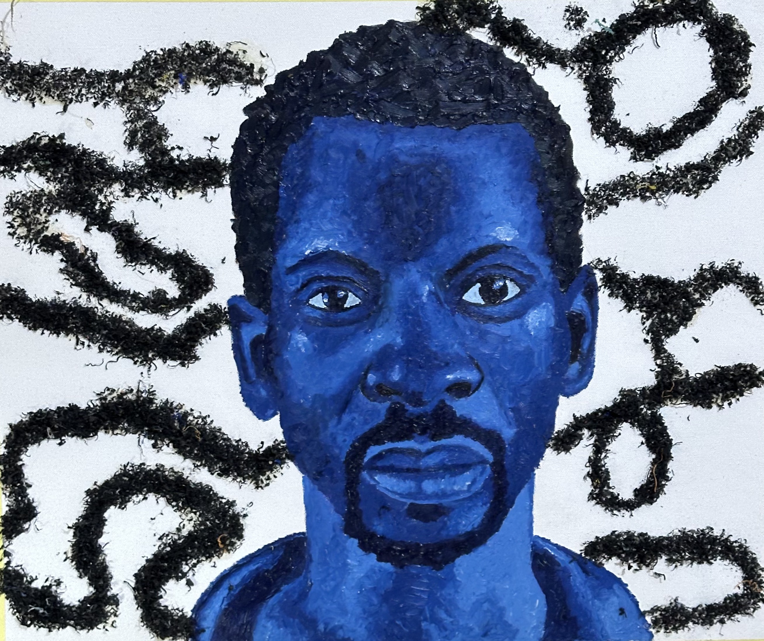 A blue-painted man facing forward amid looping black forms made with recycled plastic.