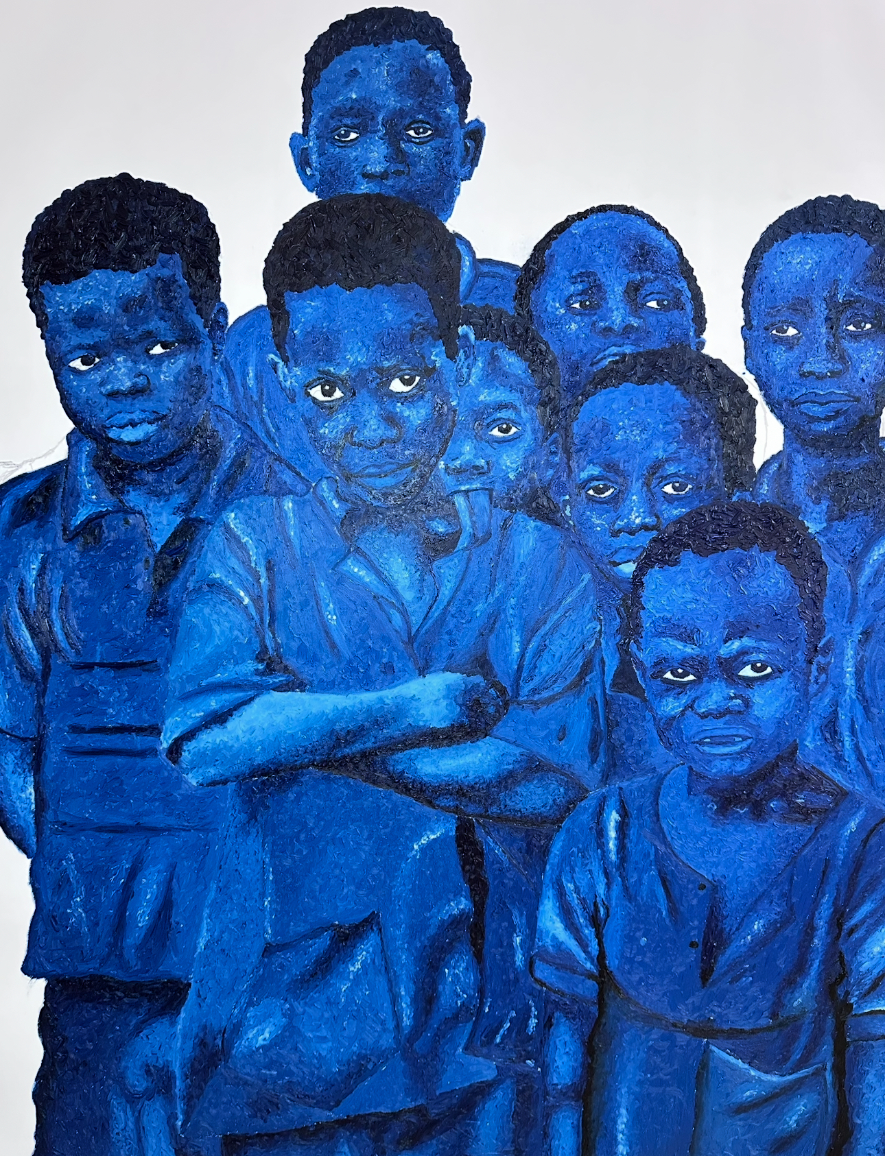 A group of nine blue-painted children gathered closely against a pale ground in El-ham Tabsoba’s painting Seven in One.